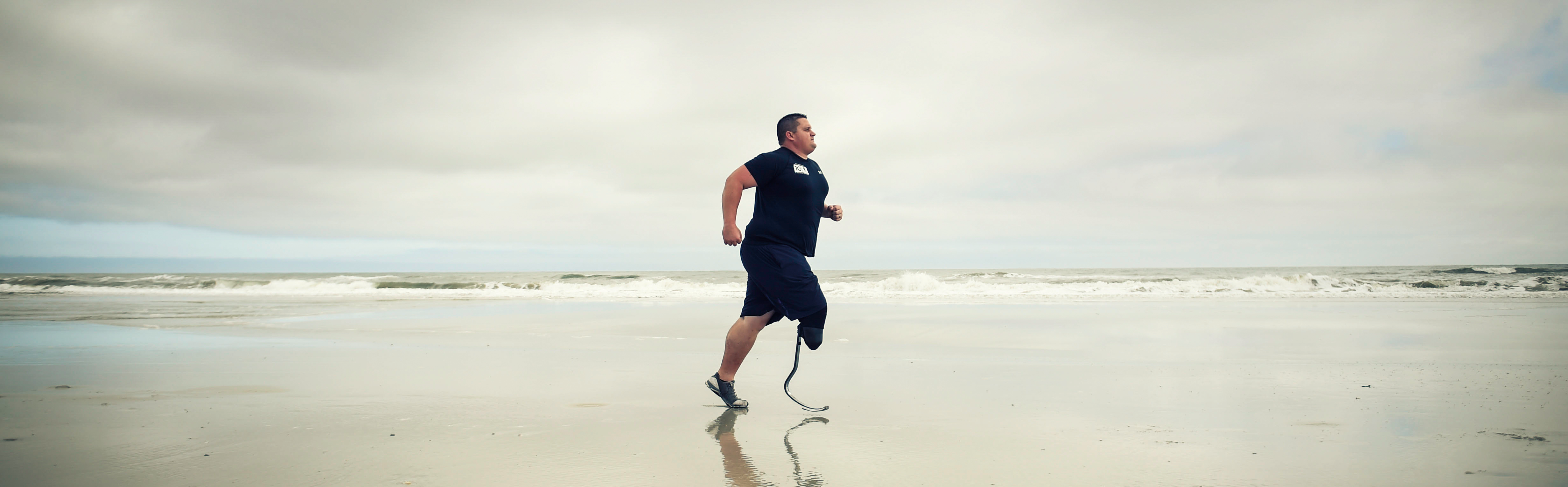 Amputee warrior running on beach with blade prosthetic